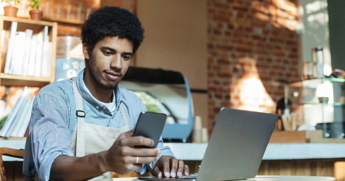 Cafe worker manages his business using a smart phone and a laptop.