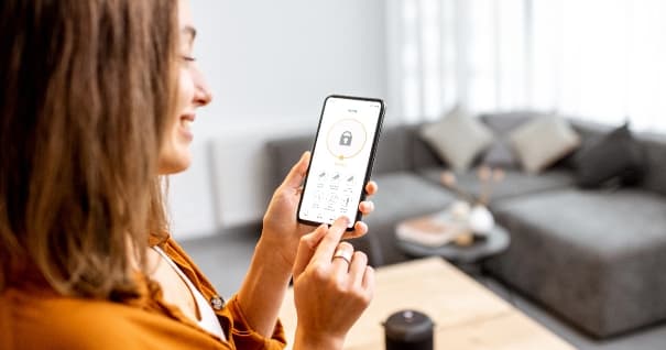 Jeune femme tenant un téléphone intelligent avec une application de sécurité lancée à la maison. Concept de contrôle et de gestion de la sécurité domestique à partir d'un appareil mobile.