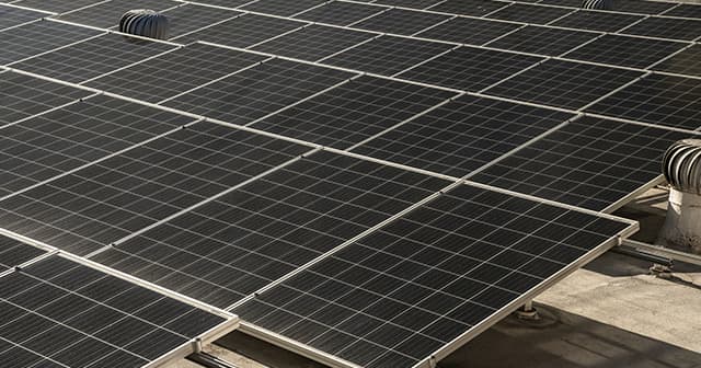 Several rows of solar panels on a roof, pointing towards the sun.