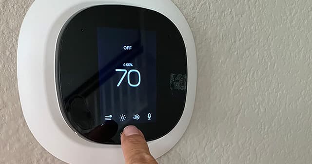 Person uses their finger to adjust the settings on a modern thermostat
