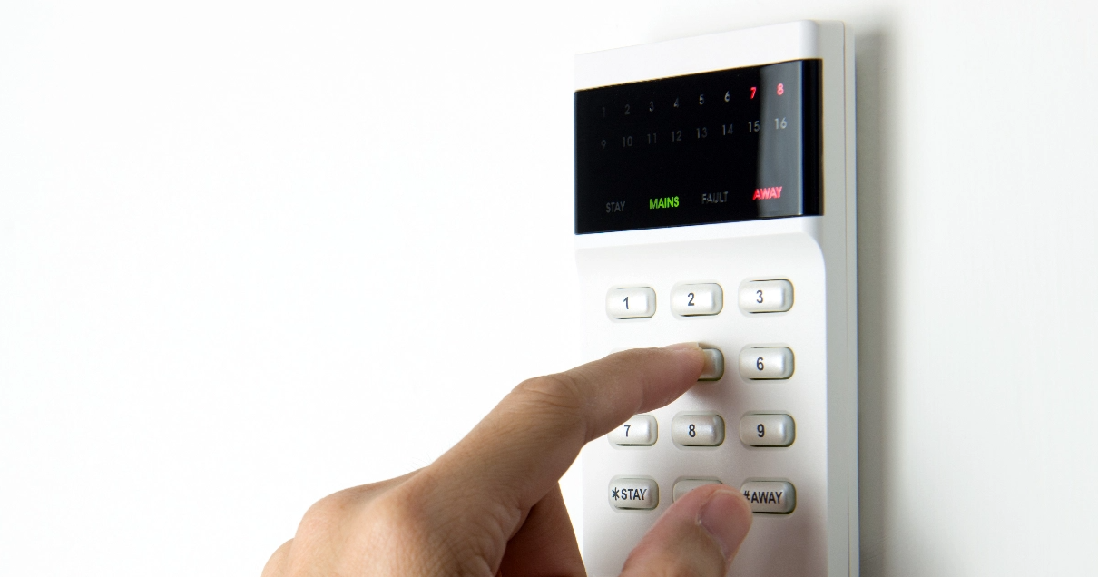 Une personne utilise ses doigts pour saisir le code sur le clavier d'un système d'alarme domestique.